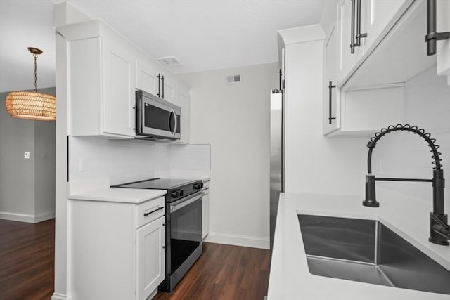 kitchen featuring appliances with stainless steel finishes, white cabinetry, sink, pendant lighting, and dark hardwood / wood-style floors