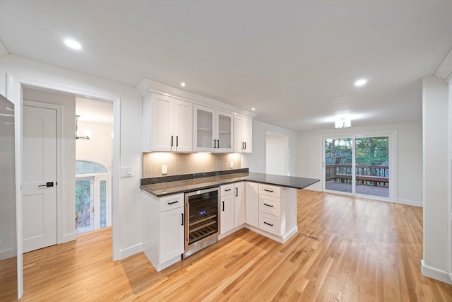 kitchen featuring wine cooler, light hardwood / wood-style flooring, backsplash, kitchen peninsula, and white cabinets