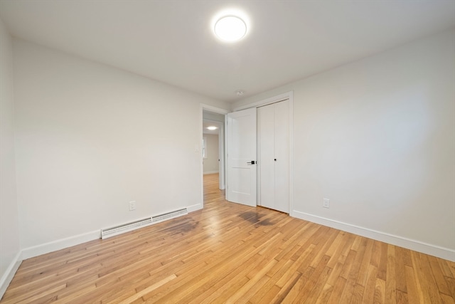 unfurnished bedroom featuring a closet, baseboard heating, and light hardwood / wood-style floors