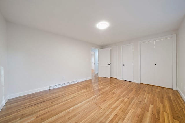 unfurnished bedroom featuring baseboard heating, light hardwood / wood-style floors, and two closets