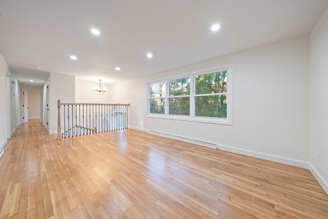 unfurnished room with a chandelier, light wood-type flooring, and a baseboard heating unit