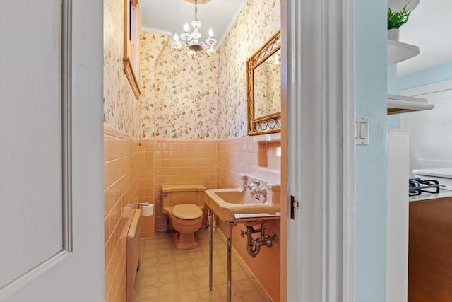 bathroom with an inviting chandelier, toilet, sink, and tile walls