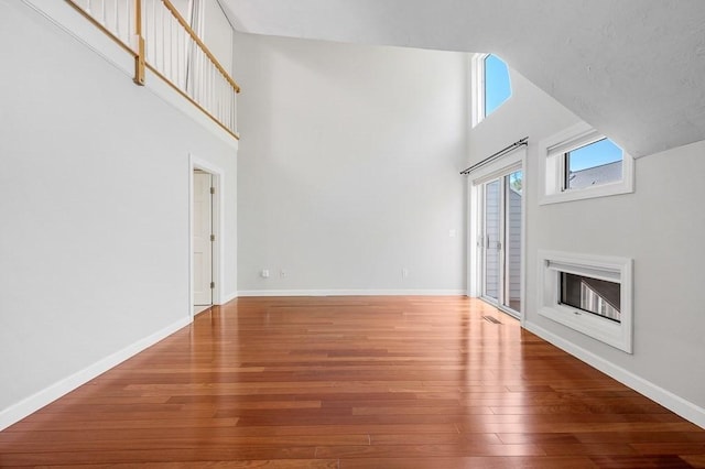 30 Eastern Point Dr Unit 30, Shrewsbury, MA 01545 - unfurnished living room featuring hardwood / wood-style floors, a towering ceiling, baseboards, and a glass covered fireplace