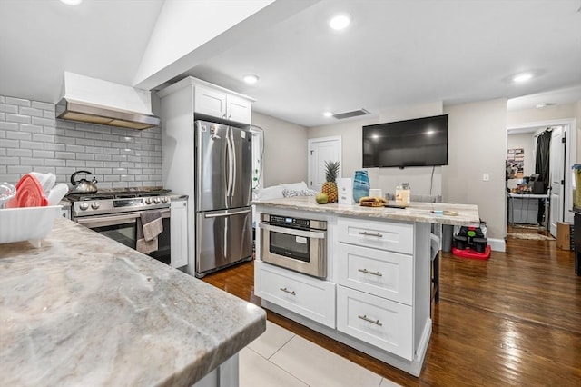 kitchen featuring white cabinets, appliances with stainless steel finishes, light stone countertops, and a kitchen breakfast bar