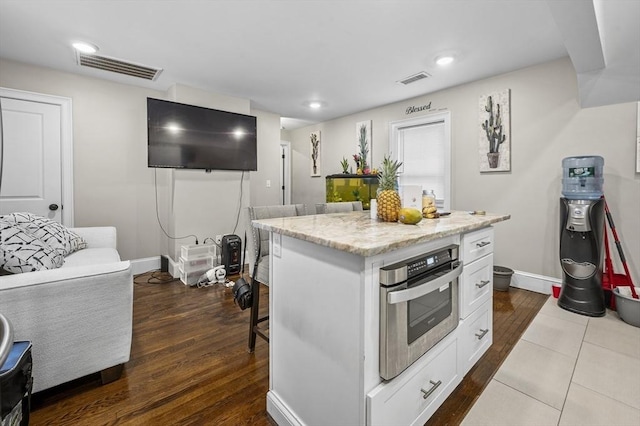 kitchen with a kitchen bar, white cabinetry, hardwood / wood-style flooring, a center island, and oven