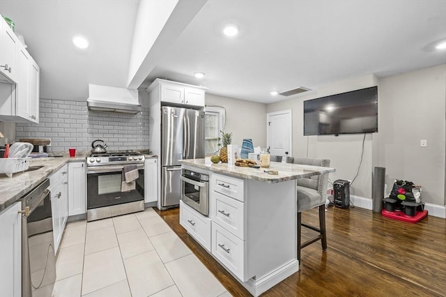 kitchen featuring white cabinetry, stainless steel appliances, light stone counters, decorative backsplash, and a breakfast bar