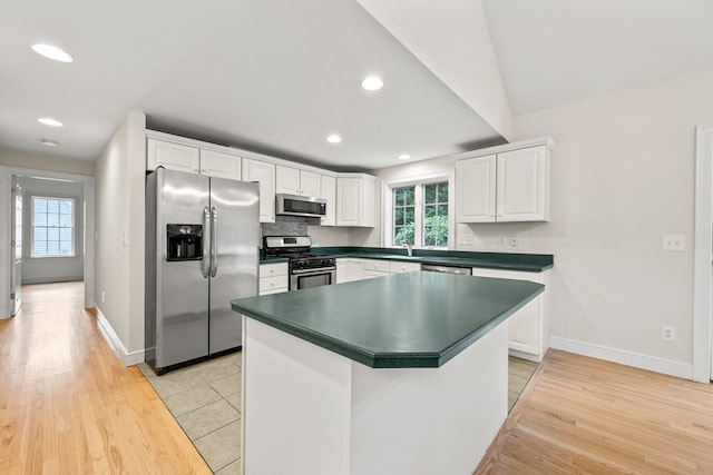 kitchen with lofted ceiling, white cabinetry, light hardwood / wood-style floors, backsplash, and stainless steel appliances