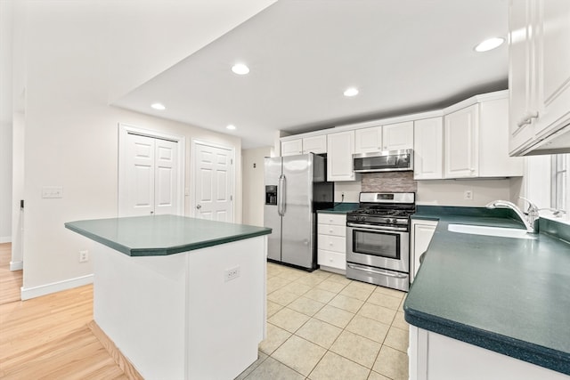 kitchen with appliances with stainless steel finishes, white cabinetry, light hardwood / wood-style flooring, sink, and a kitchen island