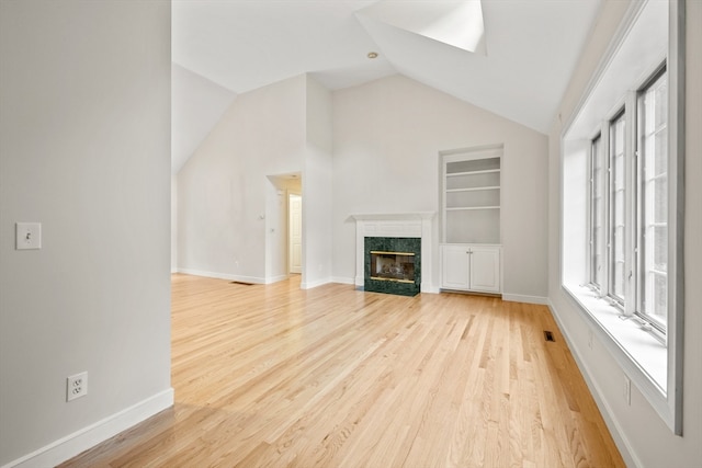 unfurnished living room featuring a high end fireplace, light wood-type flooring, lofted ceiling, and built in features