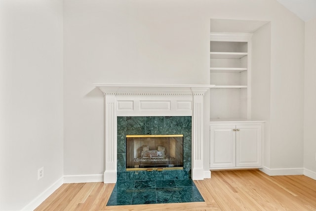 room details featuring a tiled fireplace, built in features, and hardwood / wood-style floors