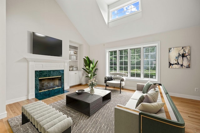 living room featuring a high end fireplace, light hardwood / wood-style flooring, high vaulted ceiling, and built in shelves