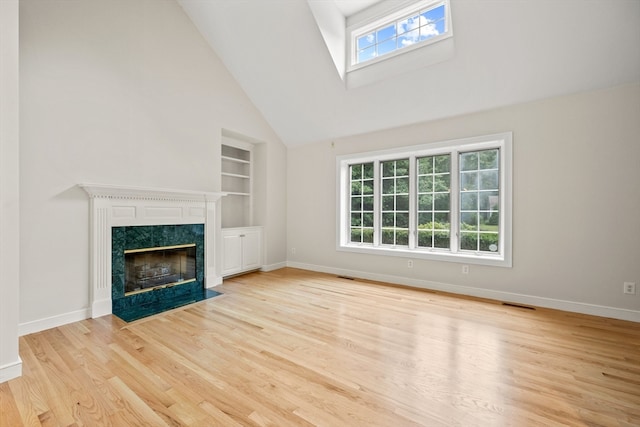 unfurnished living room with high vaulted ceiling, built in shelves, a premium fireplace, and light hardwood / wood-style floors