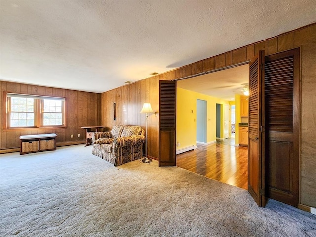 carpeted living area featuring a baseboard heating unit, wood walls, a textured ceiling, and visible vents