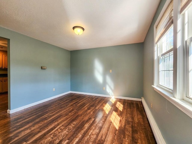 empty room with dark wood-style floors, baseboards, and a textured ceiling