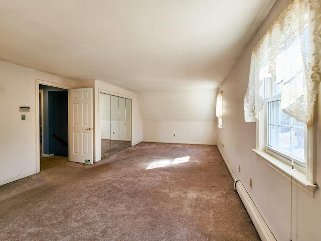 unfurnished bedroom featuring carpet floors, lofted ceiling, a closet, a baseboard heating unit, and baseboards