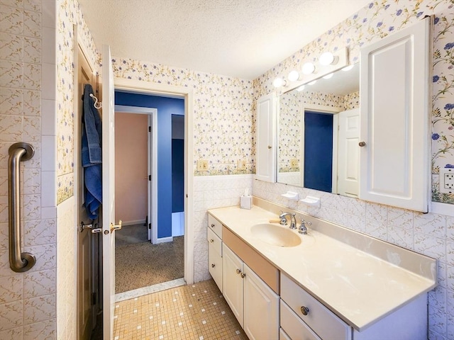 bathroom with a textured ceiling, a wainscoted wall, tile walls, vanity, and wallpapered walls