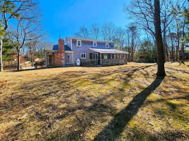 back of property featuring a lawn, a chimney, and a sunroom