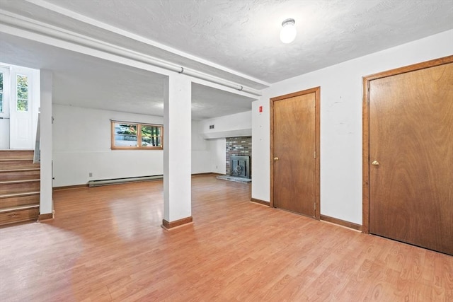 18 Bismark St, Dedham, MA 02026 - unfurnished living room with baseboard heating, a brick fireplace, light wood-style floors, plenty of natural light, and a textured ceiling
