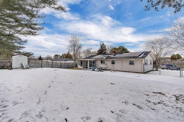 snow covered rear of property with a storage shed and solar panels