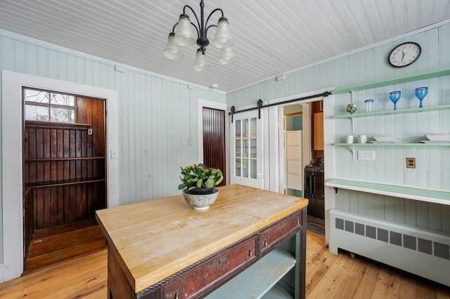 dining space featuring wooden walls, radiator heating unit, a barn door, and light wood-type flooring