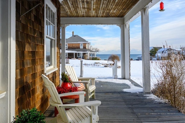 snow covered deck with covered porch and a water view