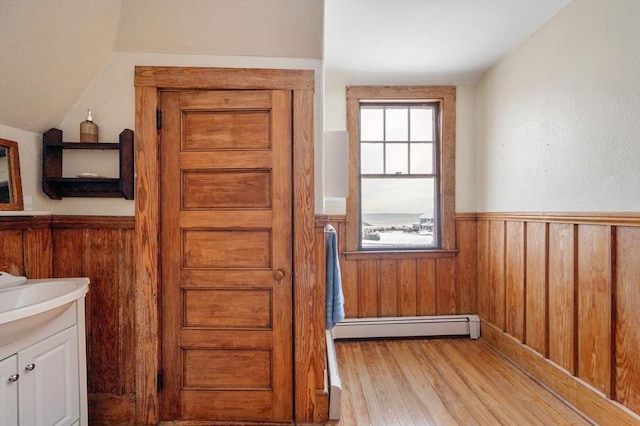 bathroom with wood-type flooring, a baseboard heating unit, vanity, wood walls, and lofted ceiling