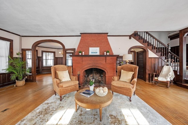 living area featuring a brick fireplace, wood-type flooring, and ornamental molding