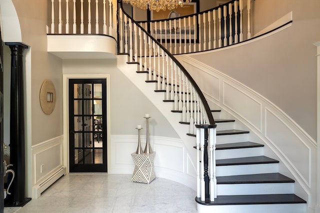 staircase with a baseboard radiator, a towering ceiling, and decorative columns