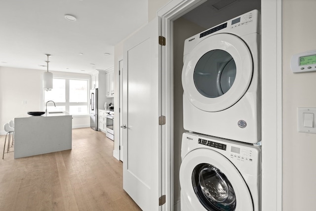 laundry area with stacked washer / dryer, sink, and light hardwood / wood-style floors