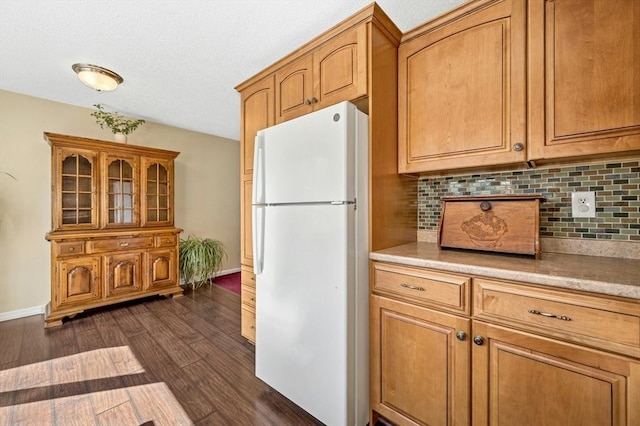 kitchen with tasteful backsplash, light countertops, freestanding refrigerator, and dark wood-type flooring