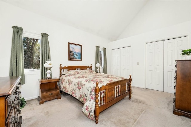 bedroom featuring high vaulted ceiling, baseboards, multiple closets, and light carpet