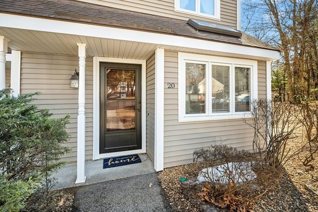 view of exterior entry with roof with shingles