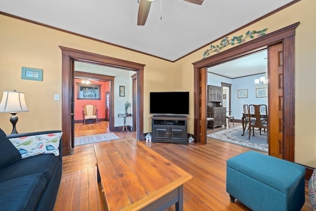 living room with baseboards, ornamental molding, ceiling fan with notable chandelier, and light wood-type flooring
