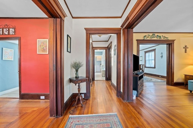 corridor with baseboards, ornamental molding, and wood-type flooring