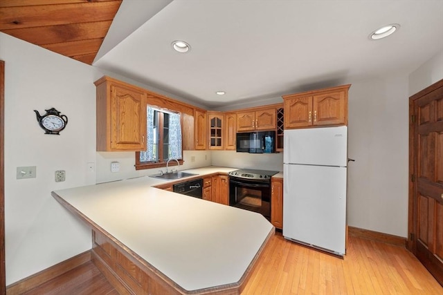 kitchen featuring a sink, baseboards, black appliances, a peninsula, and glass insert cabinets