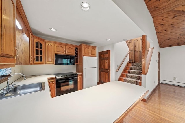 kitchen with a sink, black appliances, a peninsula, glass insert cabinets, and light wood-style flooring
