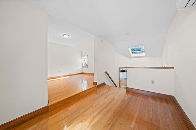 additional living space featuring baseboards, hardwood / wood-style flooring, a wall mounted air conditioner, and lofted ceiling with skylight