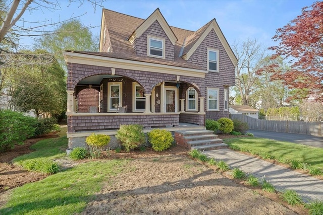 view of front of property with a porch, roof with shingles, and fence