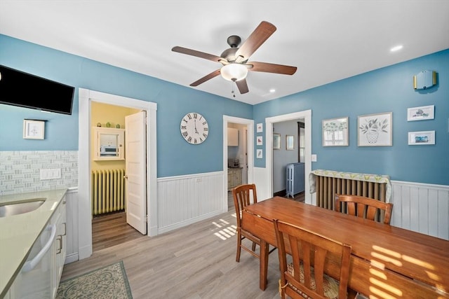 dining room featuring radiator heating unit, a wainscoted wall, ceiling fan, and light wood finished floors