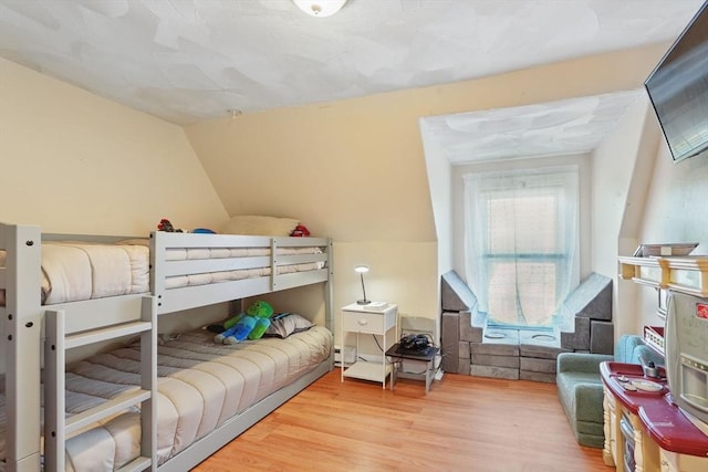 bedroom featuring a baseboard heating unit, vaulted ceiling, and hardwood / wood-style floors