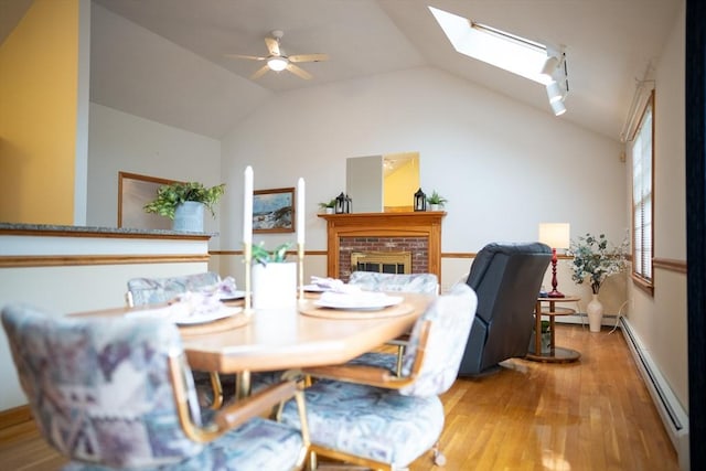 dining room with a baseboard heating unit, light wood-style floors, vaulted ceiling, a skylight, and a ceiling fan