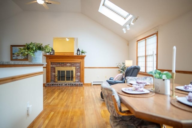 dining room featuring baseboard heating, vaulted ceiling, light wood-style flooring, a brick fireplace, and ceiling fan