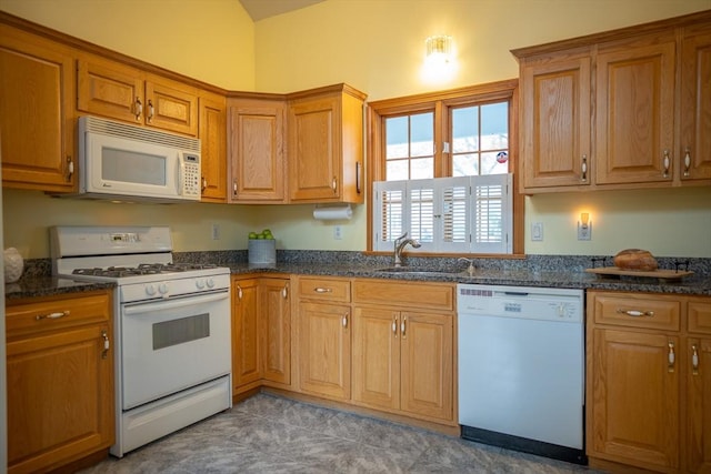 kitchen featuring white appliances, a sink, brown cabinetry, and dark stone countertops