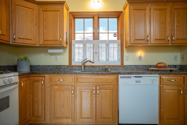 kitchen with white appliances, a sink, dark stone counters, and brown cabinetry