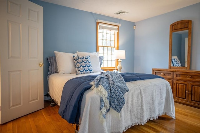 bedroom with wood finished floors and a baseboard heating unit