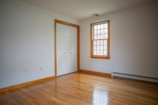 unfurnished bedroom featuring light wood-type flooring, baseboards, baseboard heating, and a closet