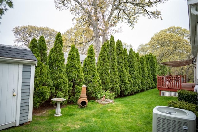 view of grassy yard featuring central AC, a deck, an outdoor structure, and a storage unit
