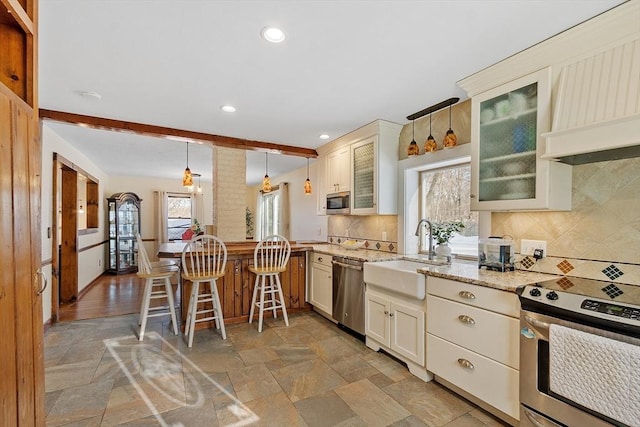 kitchen featuring stainless steel appliances, decorative light fixtures, light stone countertops, sink, and tasteful backsplash