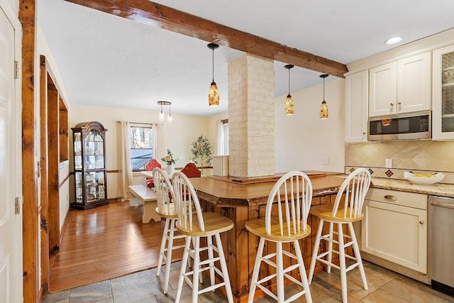 kitchen featuring appliances with stainless steel finishes, beam ceiling, light stone counters, decorative light fixtures, and backsplash