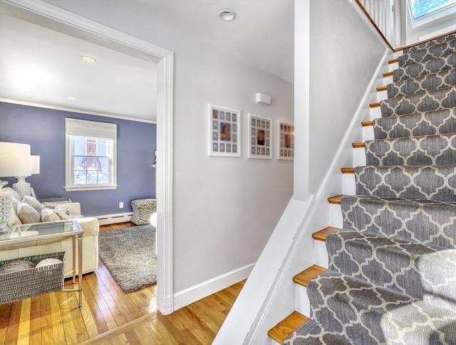 stairway with a baseboard heating unit, wood-type flooring, and ornamental molding